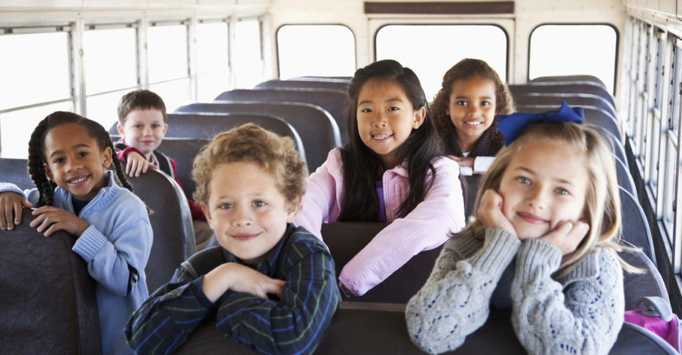 Multi-ethnic school children (ages 5 to 9) inside school bus.  Focus on Asian girl (8 years).